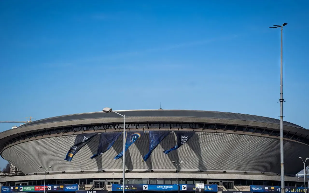 Façade d'une salle omnisports pavoisée aux couleurs d'un tournoi e-sport, sous un ciel bleu